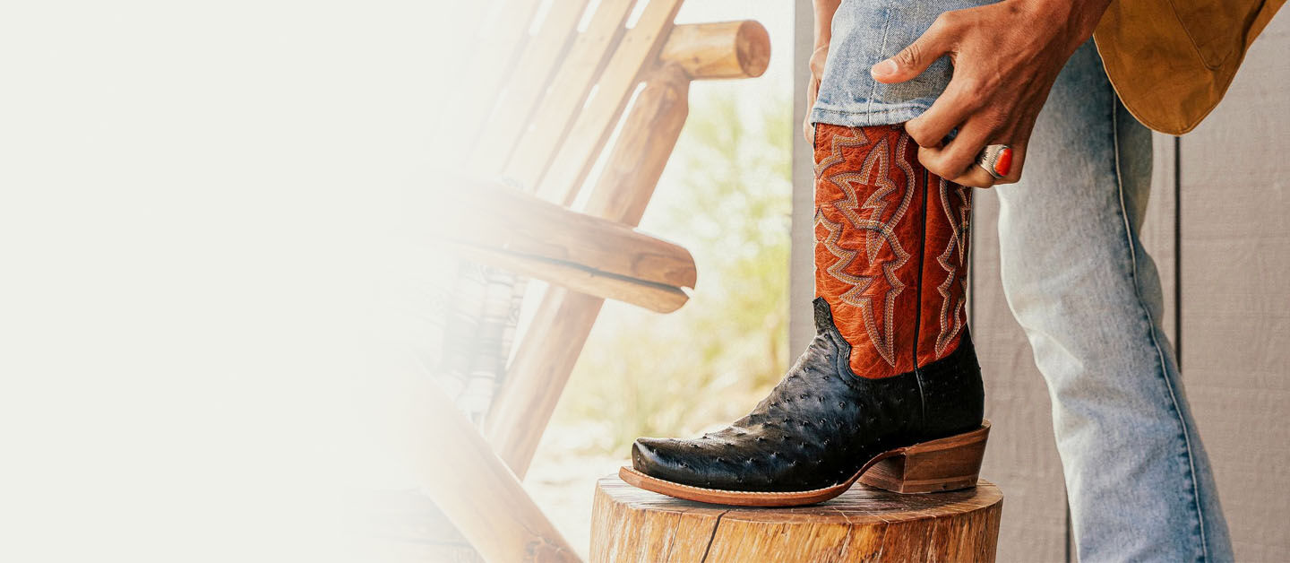 Man putting on the Rylen western ostrich boot in black and red on a stool.